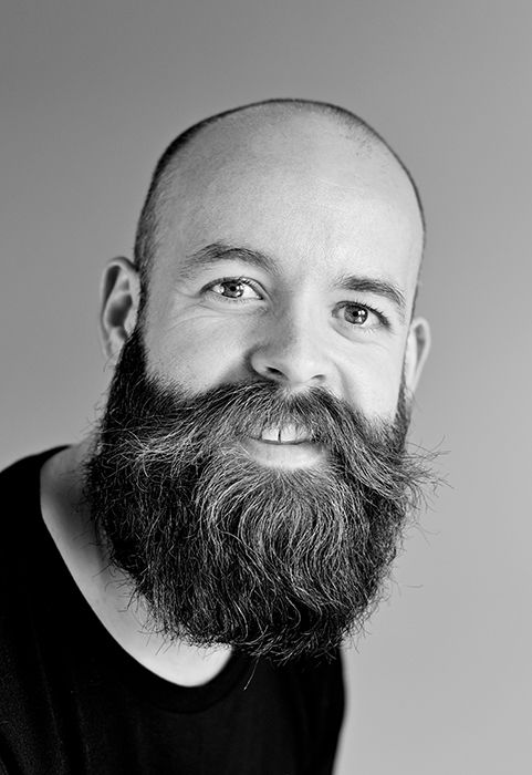 a professional black and white headshot photo of a bearded man