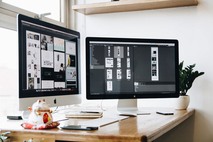 two monitors on an office desk, opening on photo editing software