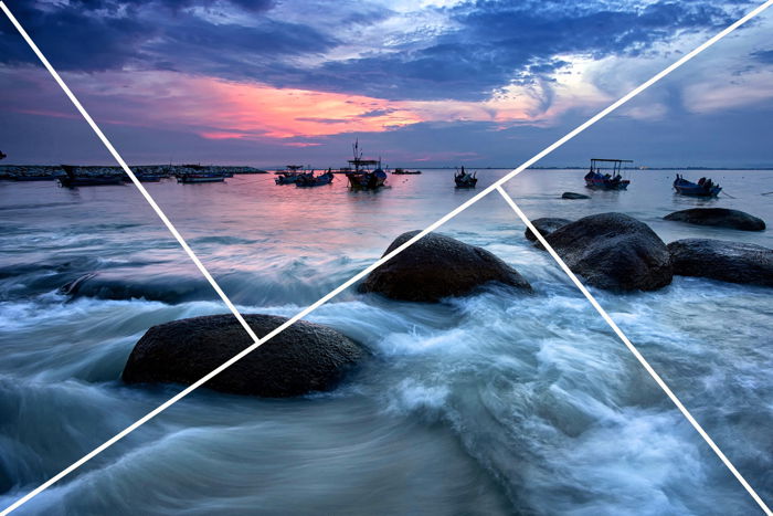 A long-exposure dusk seascape with swirling water rocks and boats in the distance with an overlay showing the golden triangle rule in photography