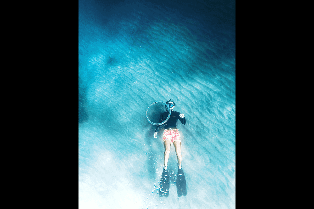 An underwater snorkeler with their back to the ocean floor for GoPro photography underwater