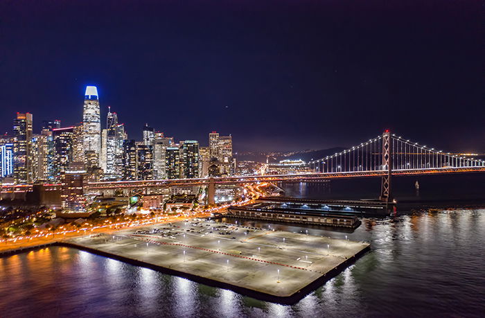 A cityscape at night with tall buildings a dock and a bridge over a river