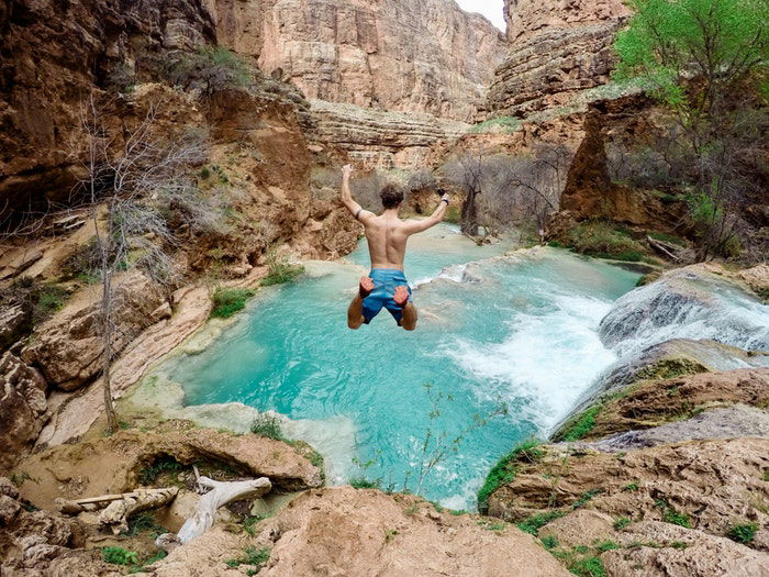 Man jumping into a pool of water surrounded by rocky mountains