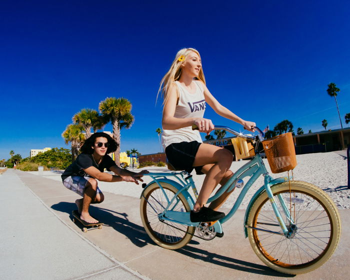 Photo of a girl riding a bike with a guy on a skateboard holding onto the bike