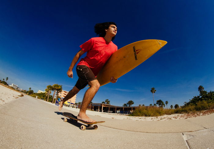 Photo of a guy with a surfboard in his hand on a skateboard