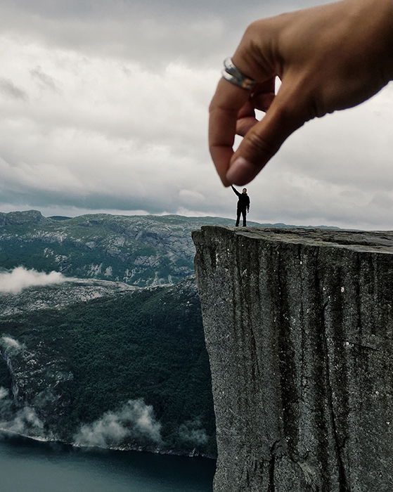 Illusion of a huge helping hand shaking a tiny climber's hand.