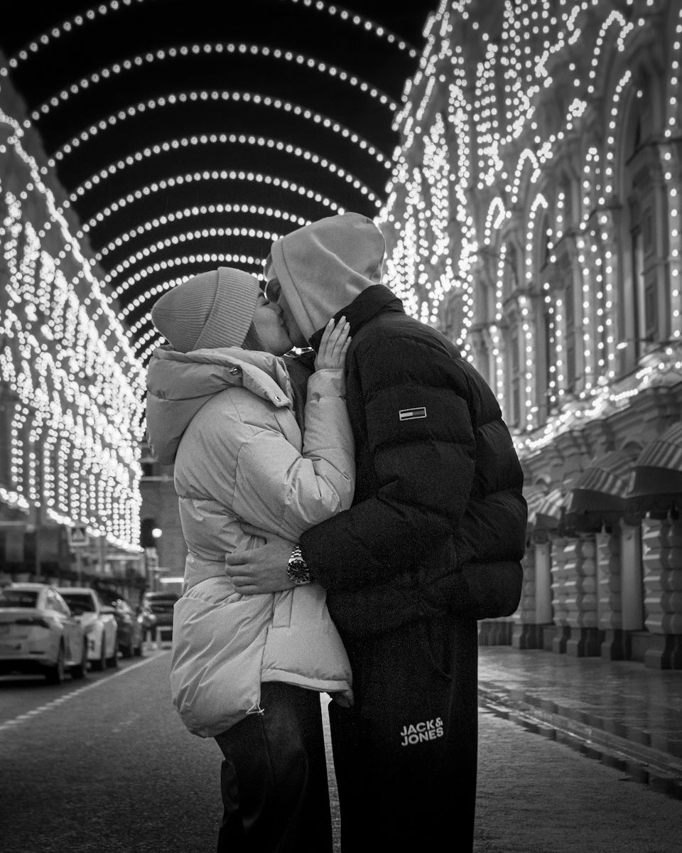 Couple kissing under white Christmas lights for couple poses