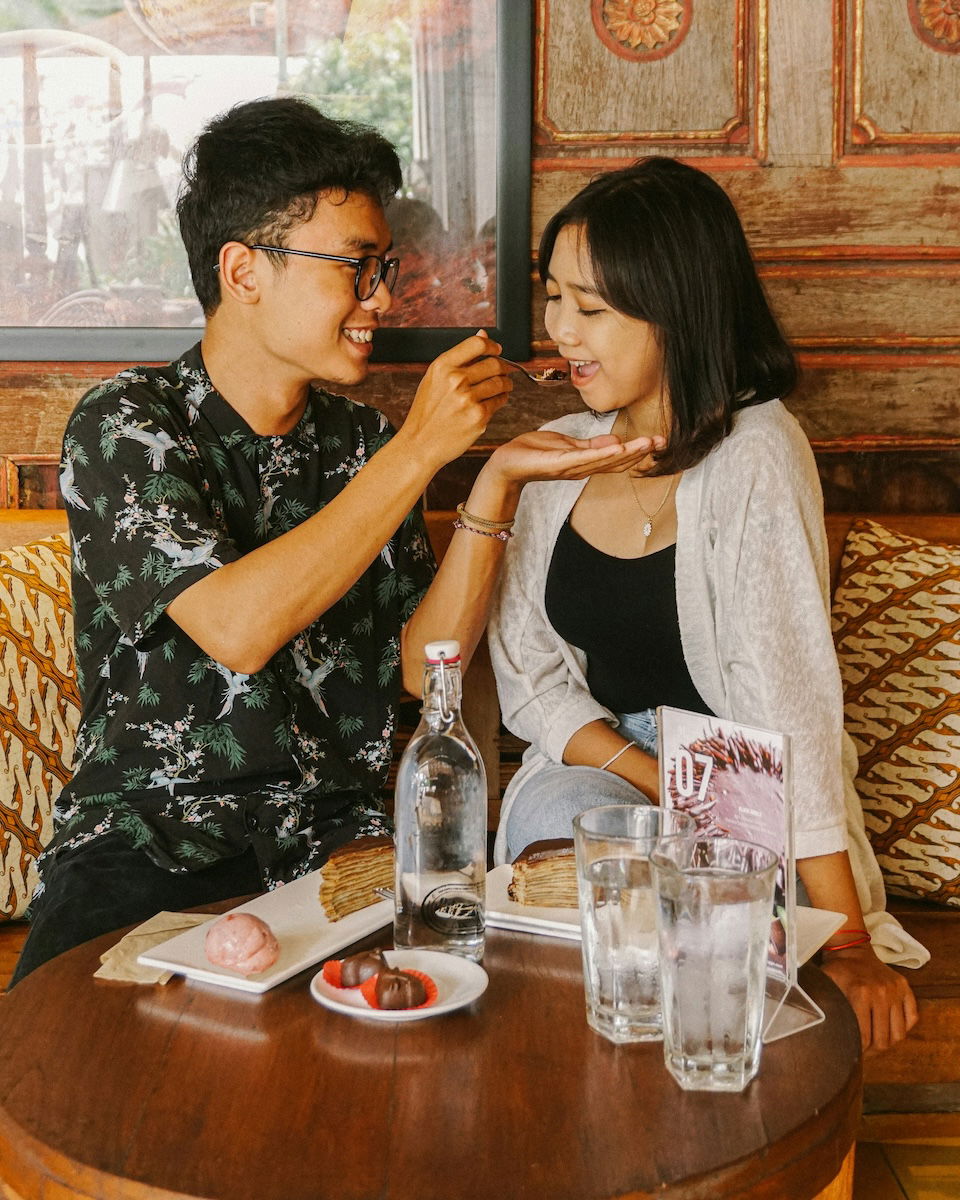 A man feeding a woman dessert at a restaurant for couple poses