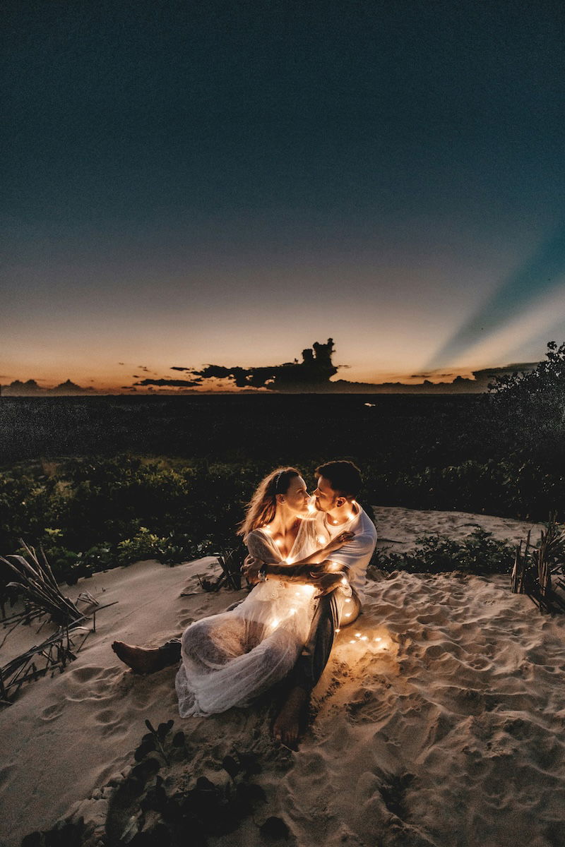 Two people sitting outside at dusk with fairy lights for couple poses