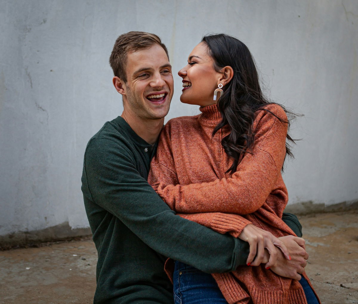 A woman whispering something in a man's ear for couple poses