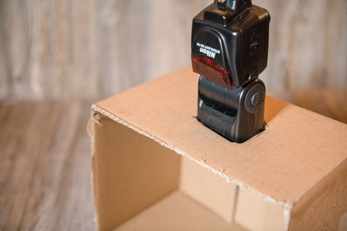 A camera flash inserted into a flap of a cardboard box