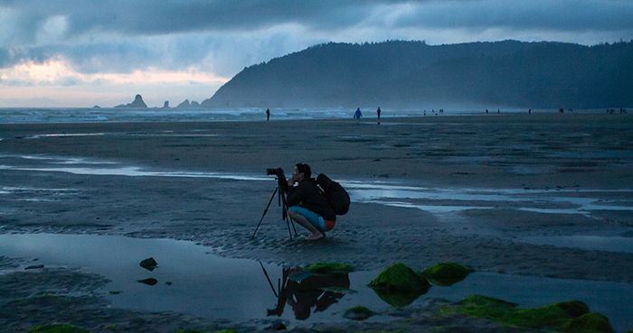 A photographer setting up tripod on a beach in low light