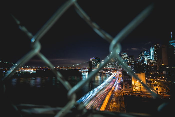 A night photography shot of a cityscape through a chain fence