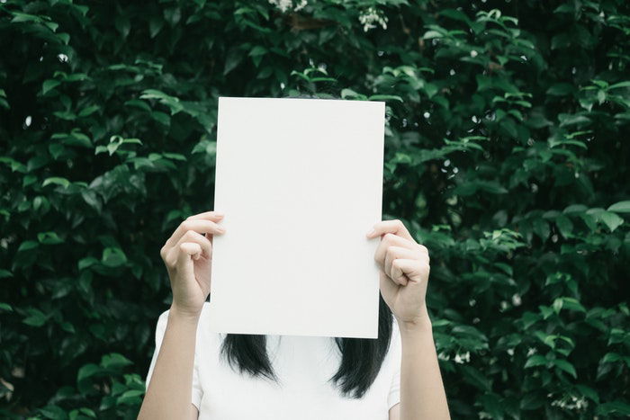 A woman holding a blank sheet of paper over her face