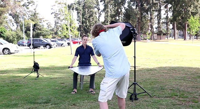 A photographer shooting a man sitting outside with a light diffuser 