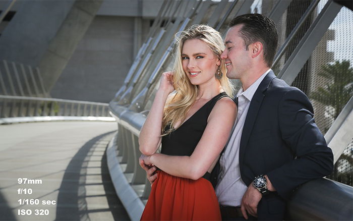 A man and a woman smiling on a bridge. 