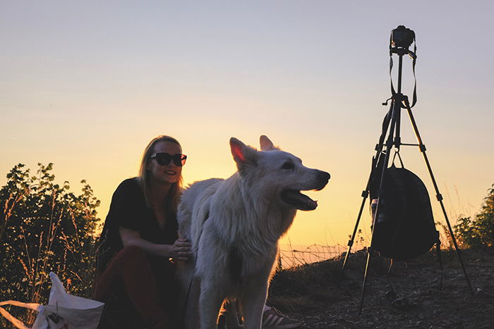 A dog and owner with a camera on a tripod at sunset set up for time-lapse photography