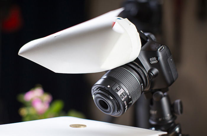 A DSLR taking a photo of a coin with a DIY photography lighting flash diffuser attached 