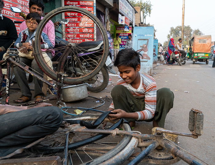 a boy changing a bicycle tire on a street in Agra, India.