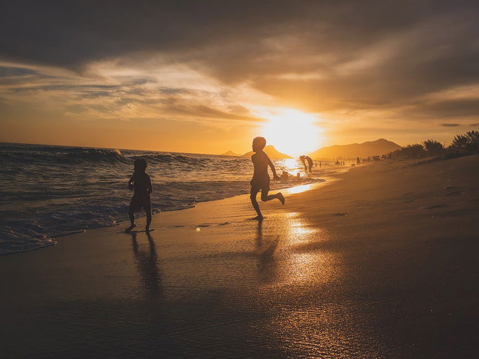 Two little boys running on a beach in low light