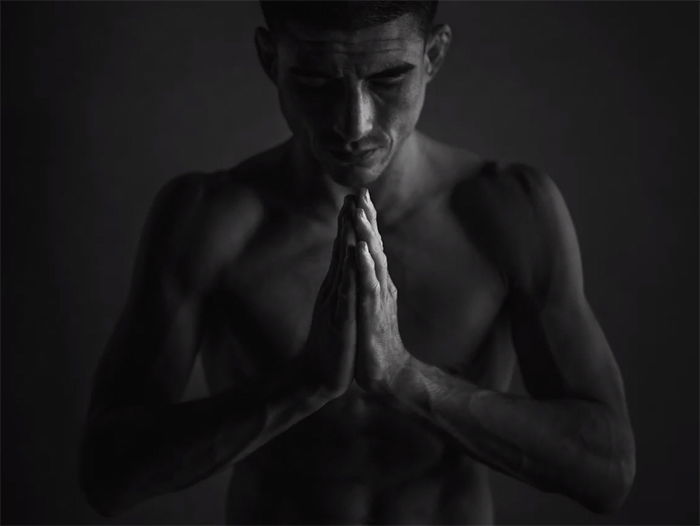 A man with his head bowed, hands clasped together in prayer or meditation pose. 