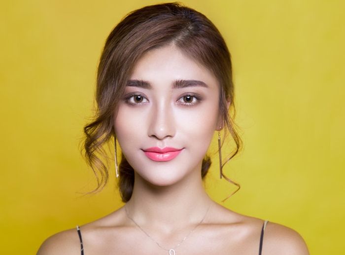 A close-up headshot of a young woman against a yellow backdrop using butterfly portrait lighting