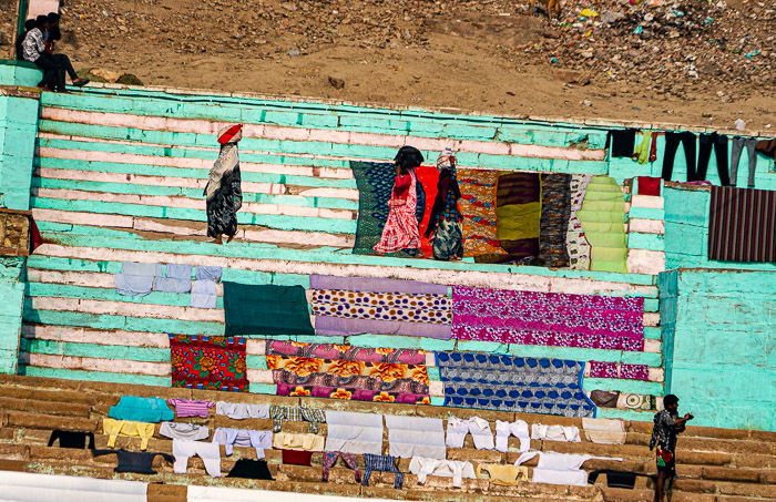 Photo of Indian women walking along painted stairs along the Ganges River. Horizon is badly tilted.