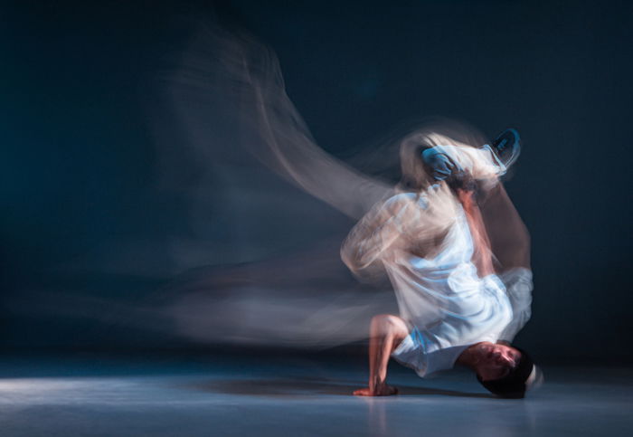 Break dancer during movement, standing on his head, with a dark background behind him. 