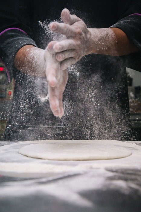 A BAKER SHAKING FLOUR ONTO DOUGH