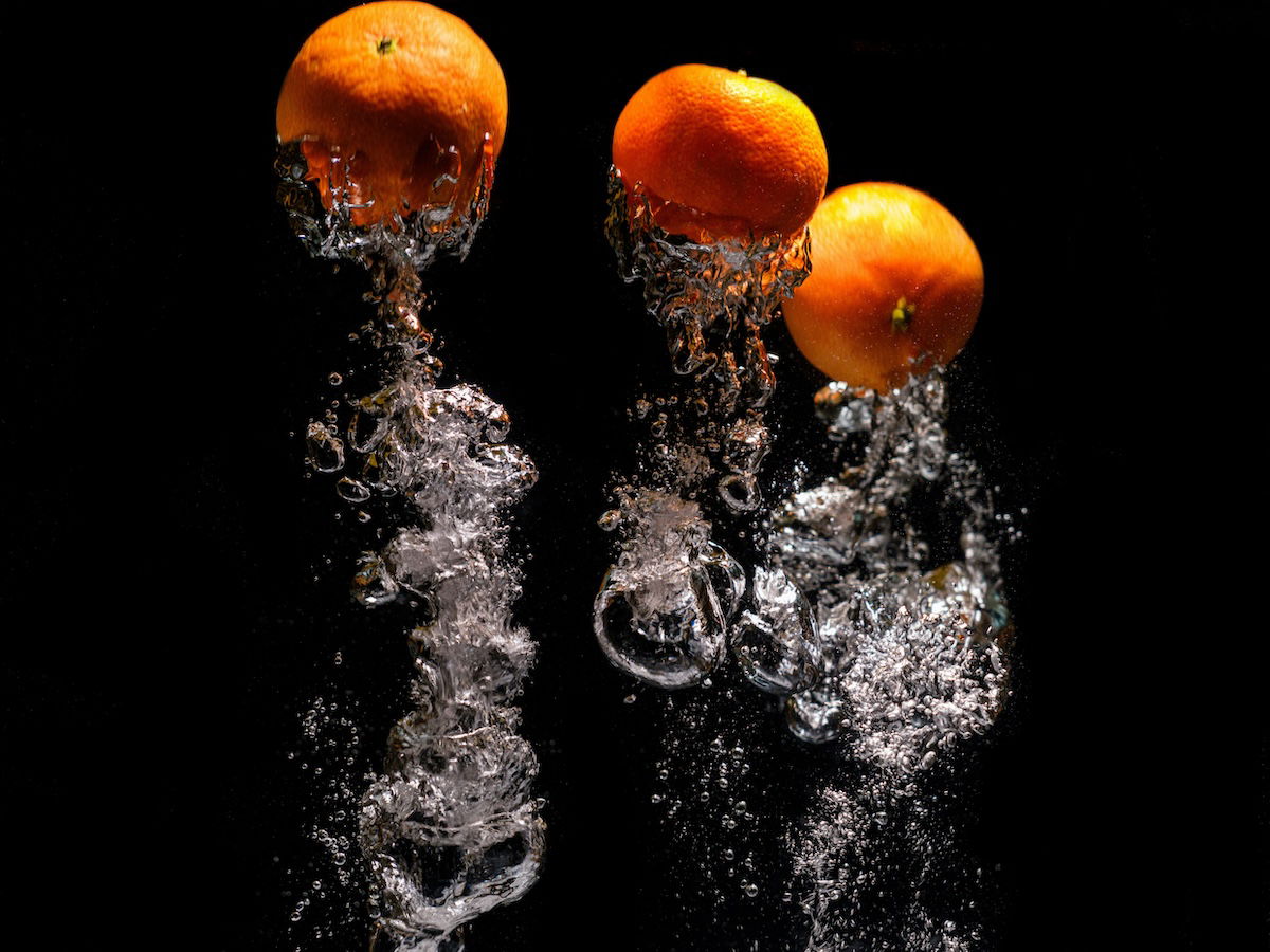 Inverted image of oranges splashed in water against a black backdrop for high-speed photography