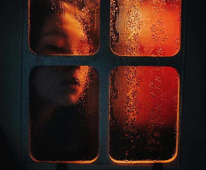 Atmospheric indoor portrait of a girl pushing her face against a window pane