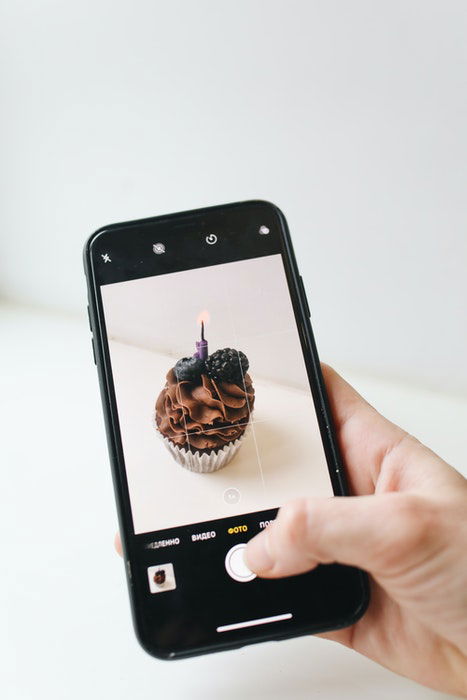 A person taking a photo of a chocolate muffin with an iphone camera