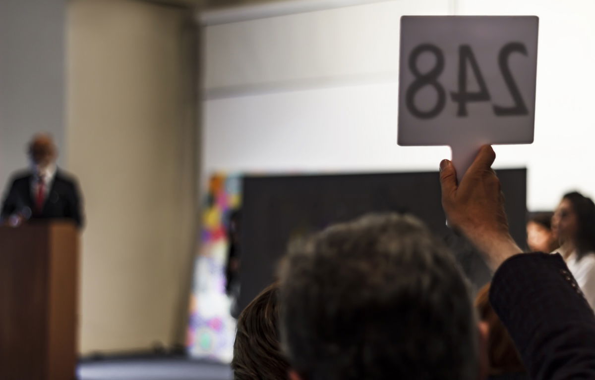 An auctioneer with a raised hand with a number on a sign to buy the most expensive photographs