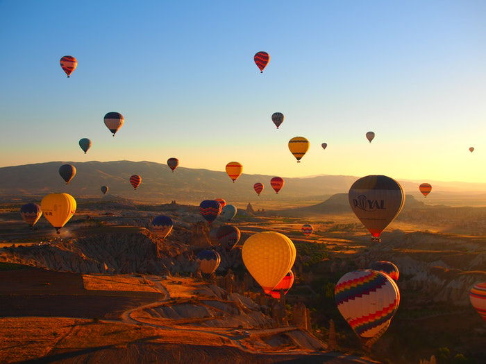 Many hot air balloons floating over a rocky landscape