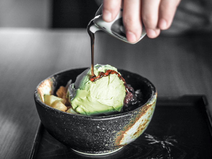 A hand pouring maple syrup onto ice cream