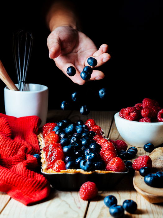 Photo of a hand dropping blueberries on a table in low key lighting