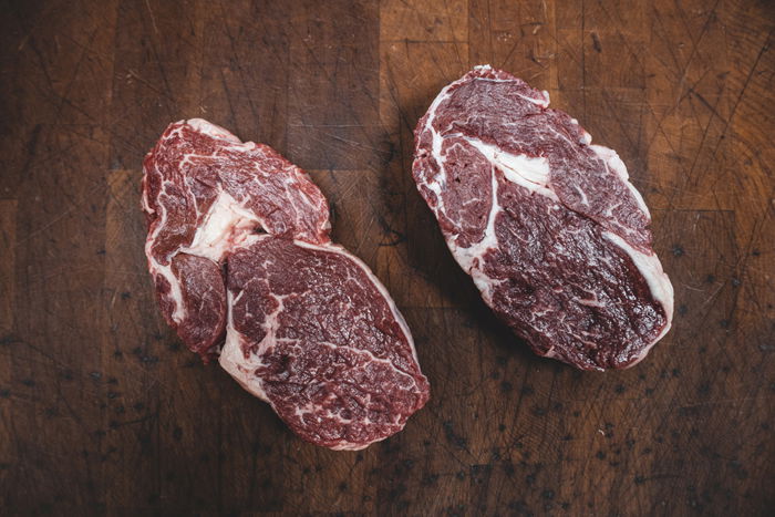 Flat lay of two cuts of raw meat on a wooden board