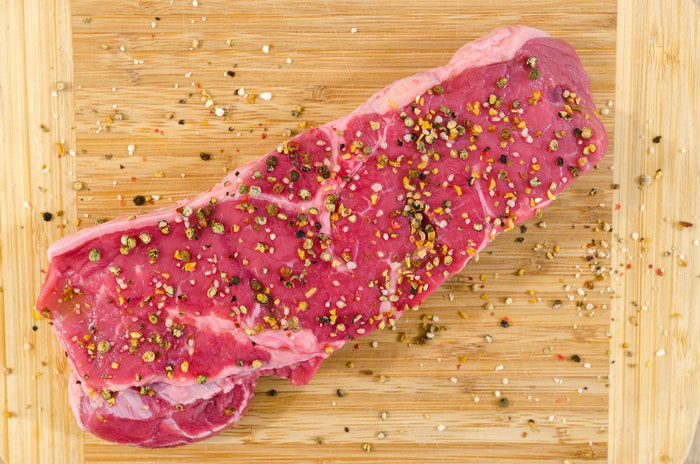 Flat lay of a seasoned cut of raw meat on a wooden board