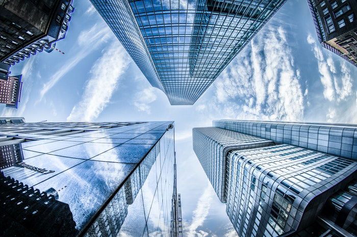 A fish-eye view of buildings with reflections rising into a blue sky with white clouds as an example of perspective in photography