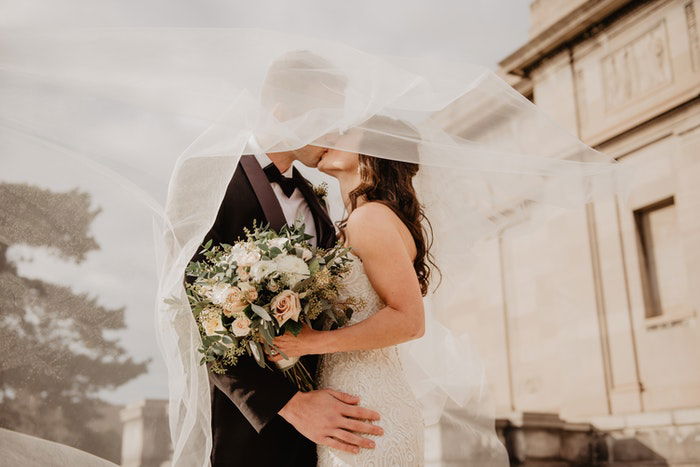 Dreamy wedding portrait of the newlyweds kissing under the brides veil