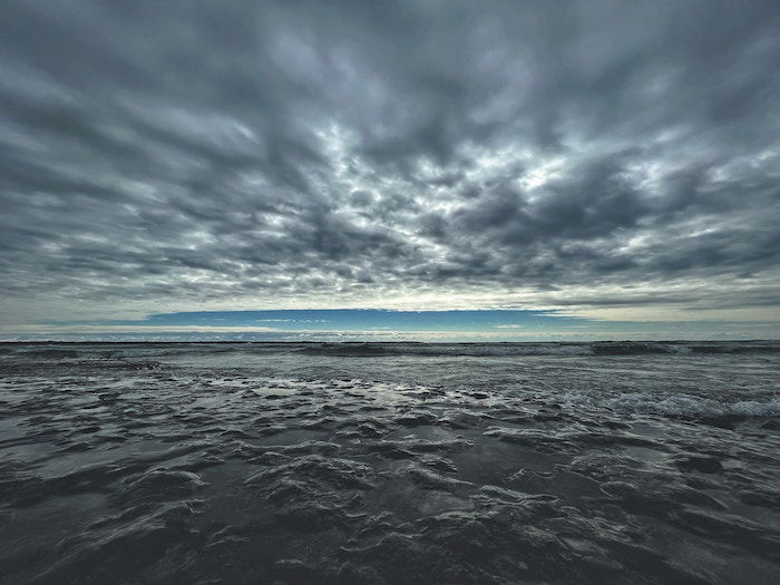 Cloudy sky mirrored by a similar-looking flat landscape by the sea