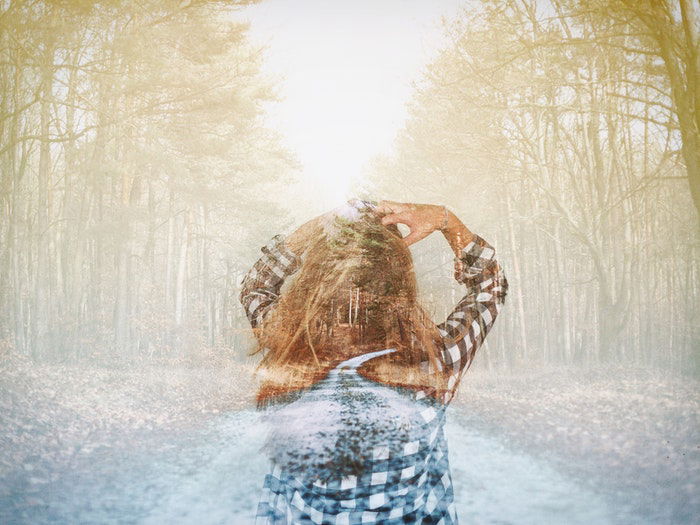 A double exposed image of a girl walking through a forest