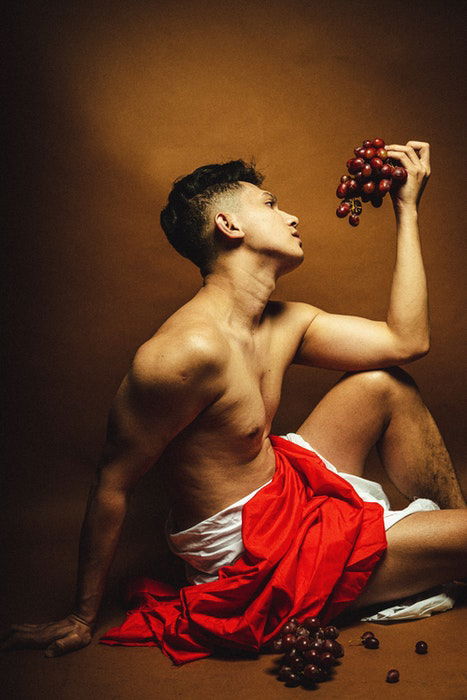 Photo of a male model in an ancient Greek-style pose with a grape