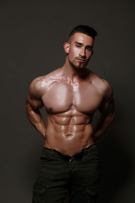 Boudoir photo of a half-naked male model standing in fron of a neutral background