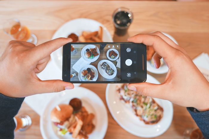 Hands holding a phone with a camera app open above plates of food for smartphone photography