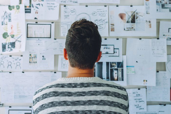 A man looking at moodboards and notes pinned to a wall