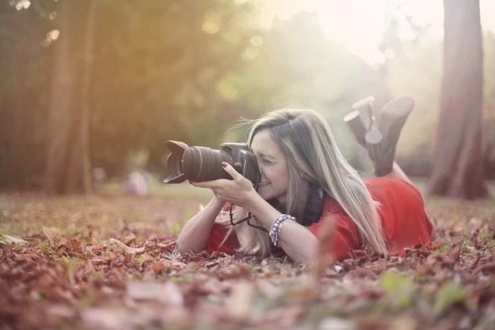 A girl lying in autumn leaves to take a photo with a DSLR