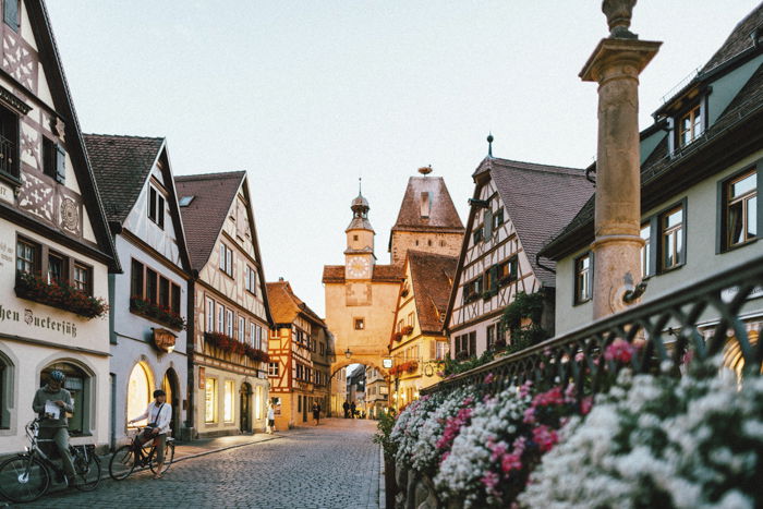 An old-fashioned European village street at dusk with illuminated shop fronts and traditional German-style houses.