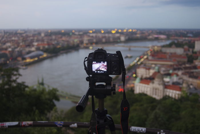 A scene of a cityscape at night, with a photographer taking a shot through a tripod. 