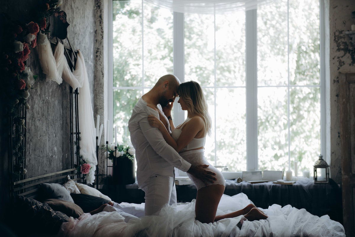 Man and woman kneelingn on a bed beside a window for couples boudoir phototgraphy