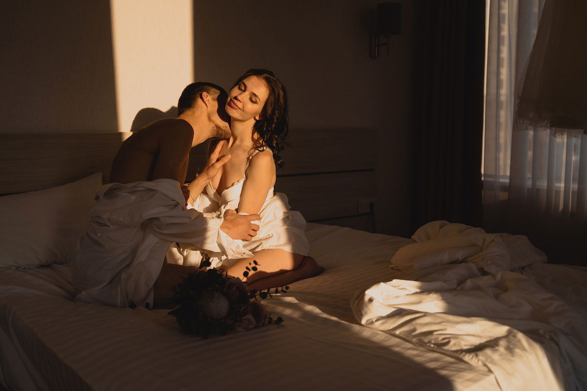 Man kissing woman on neck while sitting on bed for couples boudoir photography